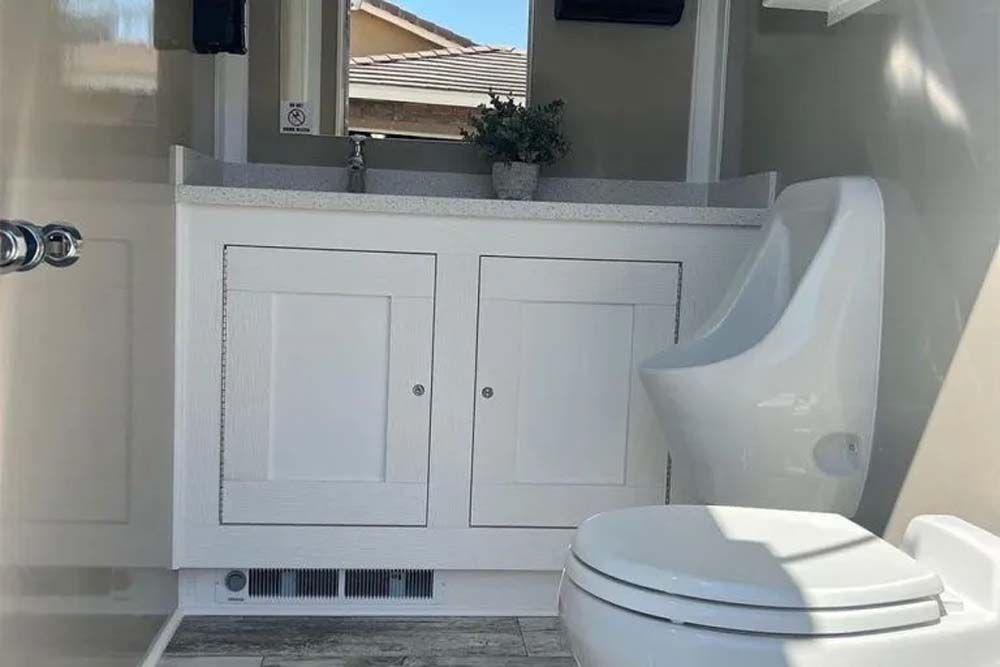 Luxury restroom trailer interior with sink, cabinets, urinal and toilet