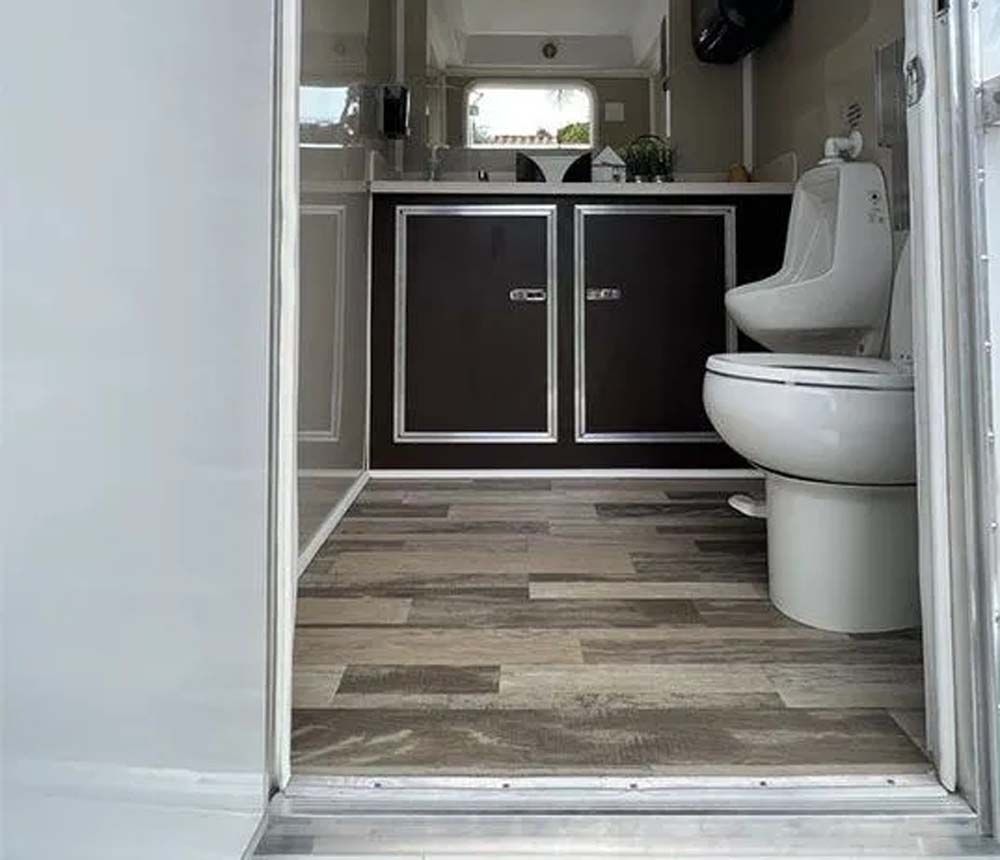 Restroom trailer interior with wood-look flooring, toilet and urinal